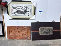 Framed block print of black horse with Asian calligraphy above two wood relief carvings depicting village and an animal figure