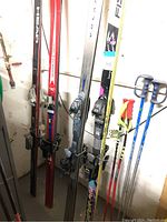 Four pairs of skis standing upright with bindings and multiple ski poles alongside in a storage area.