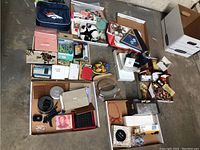 Overview of multiple small collectible items arranged on concrete floor including wallets, jewelry, decorative items, clocks, stuffed animals, model vehicles, and boxes.