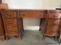 Front view of a medium-tone wood desk with nine drawers and brass-tone hardware, showing overall condition and style.
