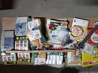 Top-down view of multiple yarn skein packs, pillow cushion kits, blue checkered fabric, embroidery hoops, tracing paper, cross-stitch fabric, craft accessories, and long ruler.