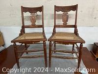 Pair of carved wood chairs with cane seats shown side by side