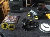 Photo showing Batman Trivia Quiz game box, Batmobile toy, Batman figure with stand, two badge pins, tin container and booklet