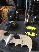 Wide view of Batman collectibles showing two metal Batarangs, two Batman logo accessories, and Spy Gear toy