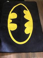 Photo of a thin black rug with a large yellow Batman logo in the center, laid flat on floor