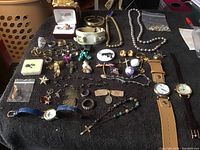 Full view of jewelry lot spread on black cloth showing rings, bracelets, necklaces, watches, and pins.