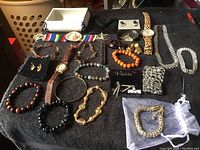 Photo showing entire assortment of jewelry including watches, earrings, bracelets, necklaces and brooches arranged on black surface.