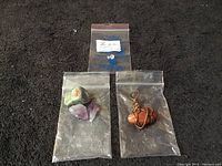 Four small plastic bags containing stones and gems arranged on a dark surface.
