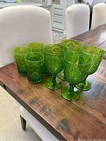 Set of eight green acrylic glasses on a wooden table includes four stemmed goblets and four shorter drinking glasses.