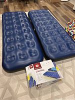 Two blue inflatable twin single-high air mattresses placed side by side on floor, with original Outbound brand packaging box alongside.