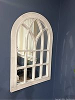 Photo of a white framed mirror with an arched top and multiple panes on a blue wall, showing light reflection and the mirror's detailed windowpane design.