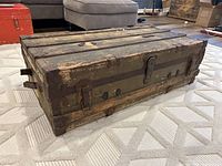 Front and side angle view of wooden antique steamer trunk showing metal bands, latch hardware and overall weathered condition