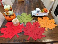 View of autumn leaf placemats, stack of decorative pumpkins, decorative candle, and pumpkin pickup truck on wooden table.