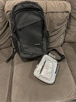 Dark grey backpack and silver side bag placed on a couch, front view showing general shape and size