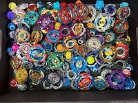 Box containing 14 assorted Beyblade tops with plastic and metal parts in various colors.