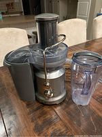 Juicer upright with wide feeding chute, metallic locking arm, and juice jug with handle next to it.