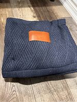 Two dark grey throws folded, showing the textured knit pattern, ribbed edging, leather patch sewn on each.