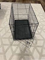 Front angled view of the black metal small folding dog crate with open front door showing latch and plastic tray inside.