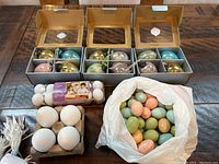 Photo showing three open boxes each containing four glass Easter egg ornaments in pastel colors, a pack of blank white paintable eggs, and a white plastic bag with pastel colored eggs.