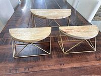 Three half circle floating shelves on a wooden table, one large and two smaller, showing the wooden tops and gold metal brackets forming triangular bases.
