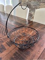 Side angle showing black metal wire fruit bowl with scrollwork and banana hanger arm.