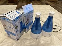 Two ultrasonic humidifiers and their boxes shown on a carpeted floor.