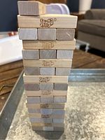 Vertical tower of wooden Jenga blocks stacked on a metal tray, showing the branded blocks and natural wood grain.