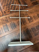 Front view of a silver metal jewellery display stand showing three horizontal bars on a rectangular base for hanging necklaces and bracelets.