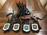 Full set of 4 wearable vests and 4 laser tag guns with charging station on wooden table.
