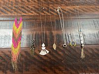 Seven long necklaces laid out on wooden surface showing variety of materials and pendants.