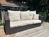 Front view of the dark brown wicker sofa with beige cushions, showing three seat and back cushions plus a small side cushion.