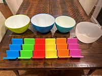 Top-down view showing four mixing bowls in assorted colors and sizes, and six colorful plastic taco holders lined up in two rows.