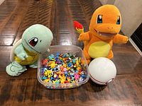 Pokémon plush toys with container of mini figurines and Poké Ball on wooden table