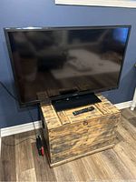 Front view of the 55-inch Sharp AQUOS TV showing the screen, bezel, and pedestal stand. Remote control placed in front of the TV on the surface.