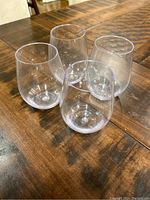 Four clear stemless acrylic wine glasses placed on a wooden table, viewed from an angle.