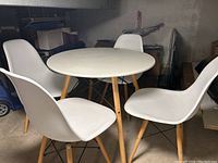 Overall view of round white table surrounded by four white chairs all with wooden legs and black metal supports.