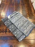Folded grey and white arrow pattern throw blanket on wooden table, showing patterned side.