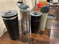 Five drink containers on wooden dining table showing lids and logos