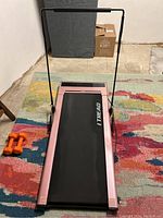 Front angle view of the ice pink I-Tread treadmill on a multicolored rug with digital display and sensor control pad, showing one side dumbbell set.
