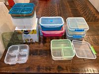 Photo showing 3 blue-lid Sistema bento boxes stacked, 2 collapsible containers, and various portion control containers with compartments visible on wooden table.