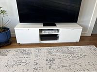 Full view of the white lacquer TV stand with TV on top, showing its overall size and style.