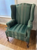 Front view of dark green striped wingback accent chair on wooden floor