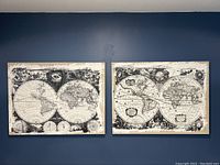 Two framed antiqued world atlas canvases mounted side by side on a dark wall.