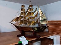 Front left perspective view of brass model ship on wood base showing hull and sails