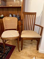 Front view of two wooden chairs side by side on wooden floor with cabinet and rug in background.