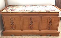 Front view of the wood storage chest featuring three floral painted front panels and cushioned floral fabric seat.