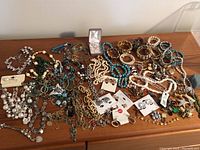 Wide view of assorted costume jewelry spread out on wooden surface, showing various bracelets, necklaces, and earrings.