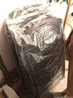 Four black metal folding chairs stacked and wrapped in clear plastic bags, showing warnings on plastic.