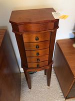 Front view of five drawer wooden jewelry chest with round metal pulls and wood legs.
