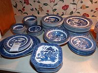 Multiple stacks of round dinnerware and bowls on counter: large dinner plates at back right, lunch plates to left, saucers under tag, square plates front center, soup and cereal bowls front left, berry bowls at back left